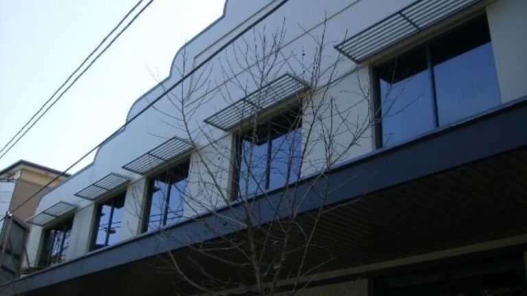 Modern slatted metal window awnings mounted above upper-floor glass windows on a building exterior.