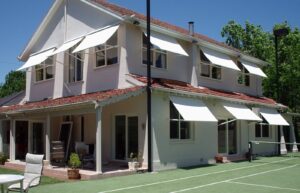 Multiple white drop arm awnings fitted over upper and ground floor windows of a two-story home.