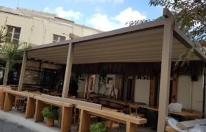 Beige motorised retractable patio roof by Shade Systems installed over a wooden outdoor restaurant patio.