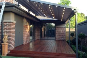 Dark grey motorised retractable roof with integrated warm LED lighting over a timber deck patio on a Melbourne home.