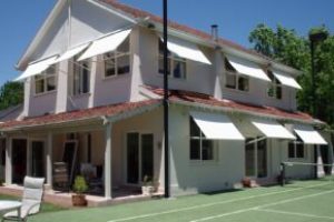 Multiple white drop arm awnings fitted over upper and ground floor windows of a two-story home.