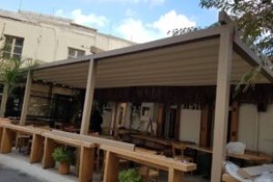 Beige motorised retractable patio roof by Shade Systems installed over a wooden outdoor restaurant patio.